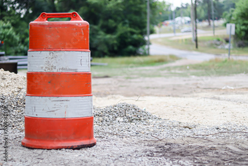 Fotografie Orange construction traffic barrel on gravel road with heavy equipment in backgr