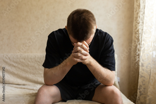 Thoughtful young man with clasped hands in close up indoors