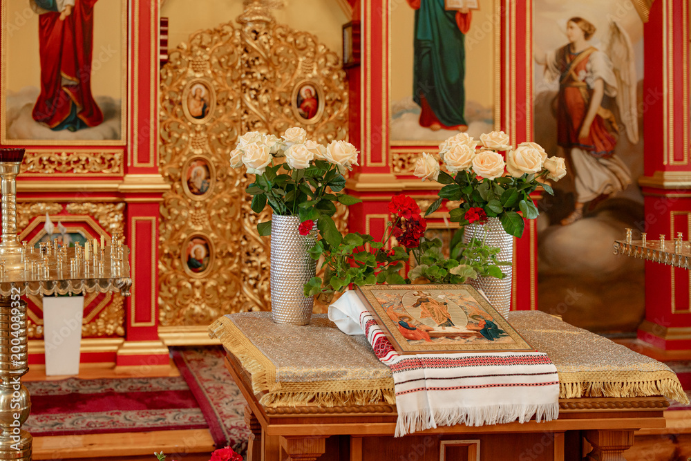 Obraz premium Religious icons and bouquets of white roses on a wooden table in an Orthodox church, sacred atmosphere, traditional worship, holy spirit.