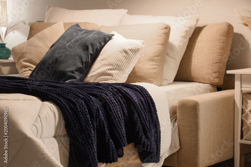 Bed with cozy blanket and soft pillows in stylish bedroom at night  closeup