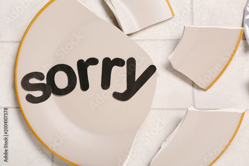 Foto Broken plate with word SORRY on white tiled table