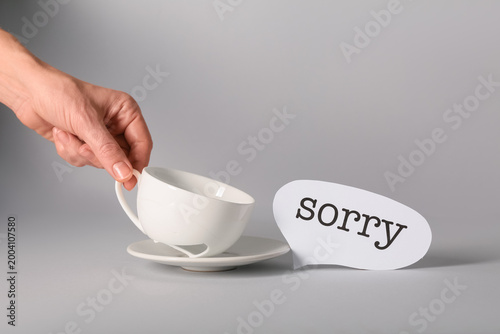 Konstfotografi Female hand with broken tea cup and word SORRY on grey background