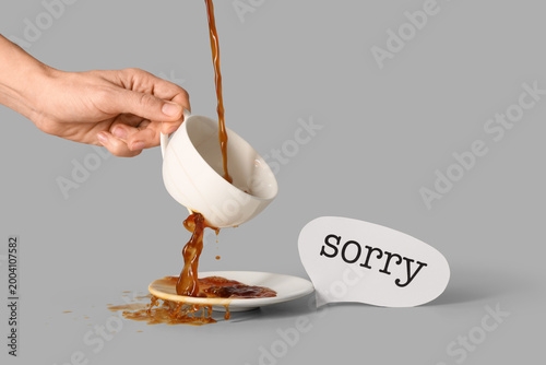Bild auf Leinwand Woman with word SORRY spilling tea from broken cup on grey background