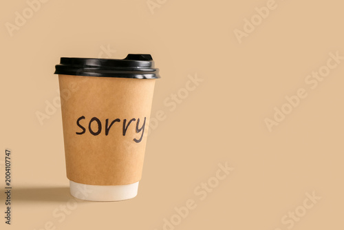 Fotografia Paper cup of coffee with word SORRY on beige background