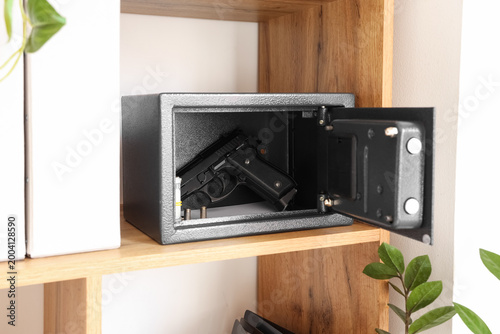 Fotografi Open safe with pistol, bullets and money on shelf at home