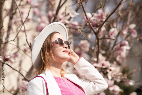 Magnolia Blossoms Woman Spring: Woman enjoys sun during spring blossom at park, wearing hat, sunglasses.