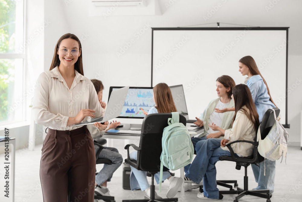 Obraz premium Female teacher with laptop and students studying at school computer lab