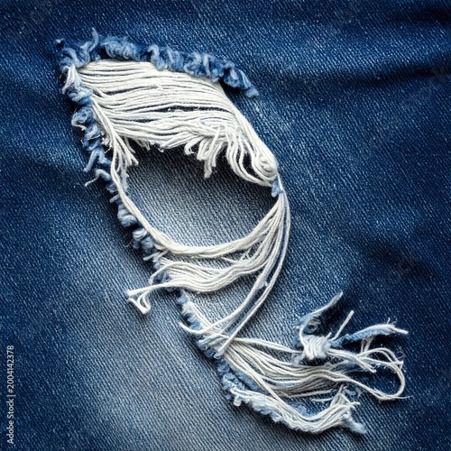 Close-up of torn blue denim fabric with fraying threads