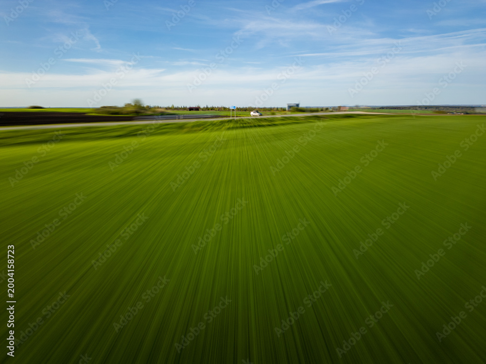 Fototapeta premium Dynamic motion blur aerial of green field and road with car