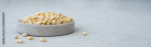 Fotografie Pine Nuts in Concrete Bowl on Light Background. Banner