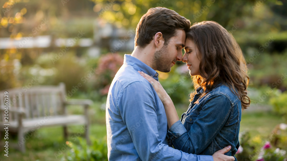 Naklejka premium Romantic couple embracing in park. Love, relationship and tenderness concept, emotional connection, warm natural light and peaceful outdoor moment.