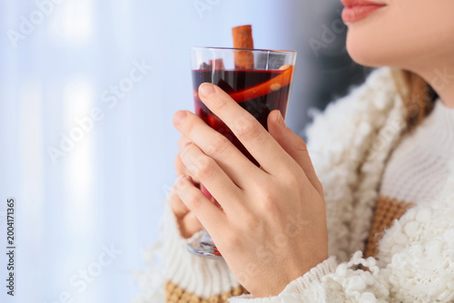 Beautiful young woman in warm sweater drinking hot mulled wine at home, closeup