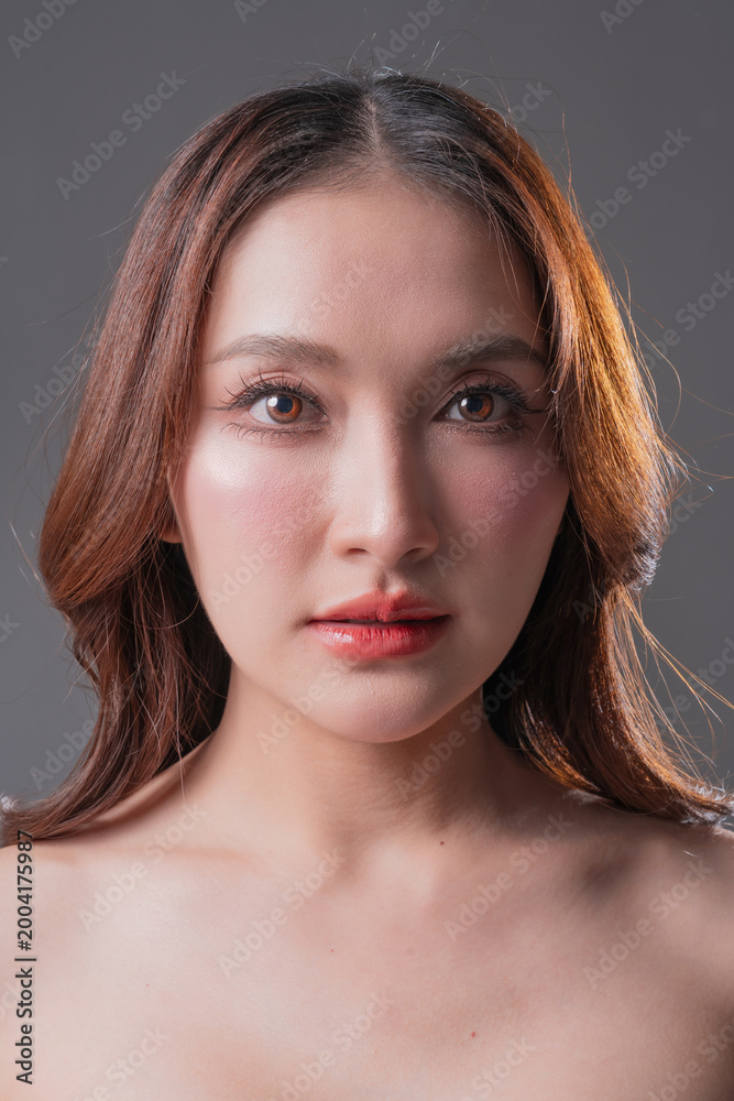 Fototapeta premium Extreme close-up beauty portrait of Asian woman with glowing skin and brown eyes, professional makeup and skincare concept on grey background