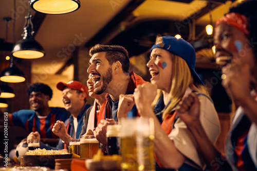 Fotografija Excited supporters cheering for their winning team while watching live sports event in pub