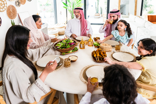 Fotografie Arab family wearing traditional saudi clothing having lunch at home - Middle-eas
