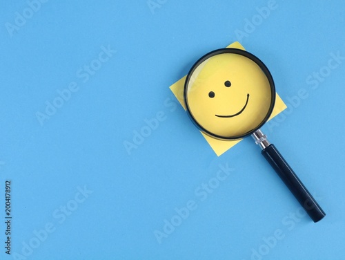 Magnifying glass with yellow adhesive note featuring hand drawn smile face. Represents customer satisfaction, positive feedback, excellent service rating, and happiness