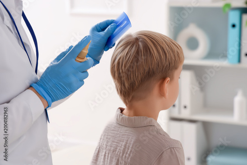 Bild auf Leinwand Female doctor with remedy brushing little boy's hair with pediculosis in clinic,