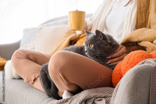 Принти на полотні Young woman with cup of tea and cute British cat sitting at home on autumn day,