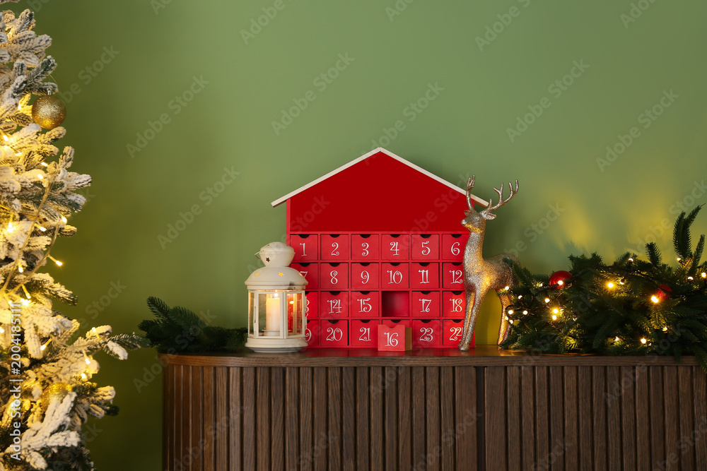 Fototapeta premium Advent calendar with lantern and Christmas wreath on drawers near green wall