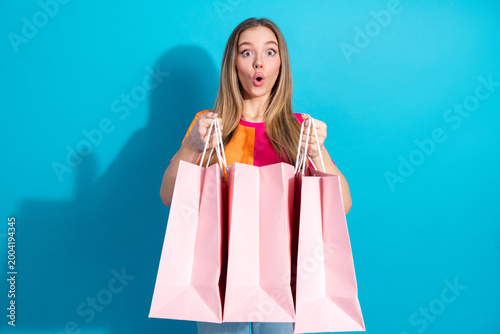 Foto Young woman with pink shopping bags excited about shopping against blue backgrou