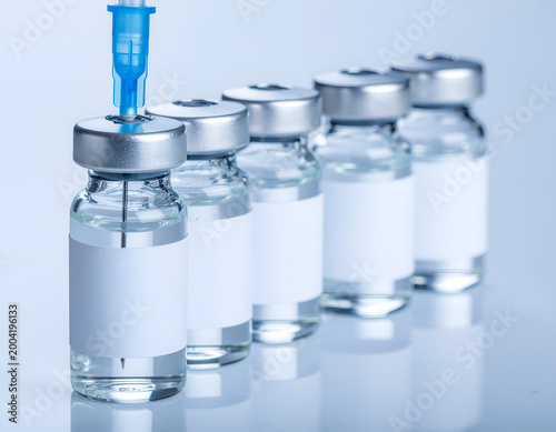 Row of sterile vaccine vials with syringe needle in medical laboratory.