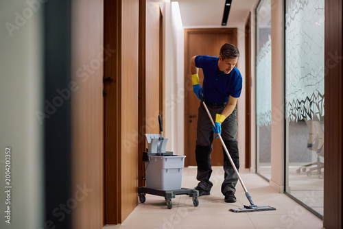 Photos Commercial cleaner using mop while cleaning office hallway.