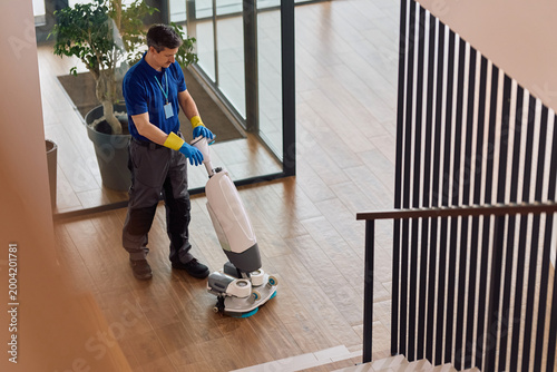Fotografia Janitor using professional floor scrubbing machine while cleaning corporate office lobby