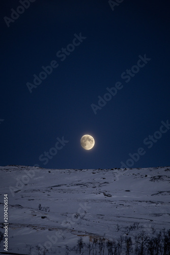 Full moon rising over snowy Arctic tundra in Kilpisjarvi, Finland