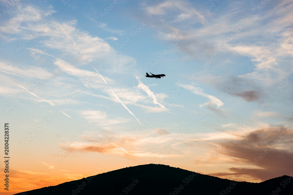 Fototapeta premium Airplane Silhouette at Sunset Over Mountain Bay