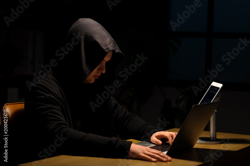 Hacker using laptop at tabl...