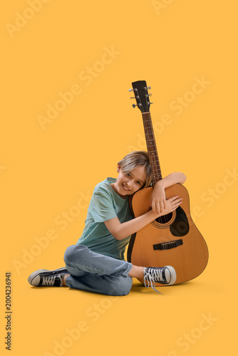 Cute little boy with guitar on yellow background