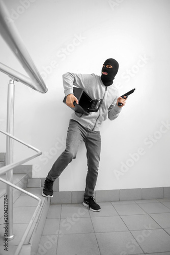 фотографія Male thief with safe and gun escaping in stairway