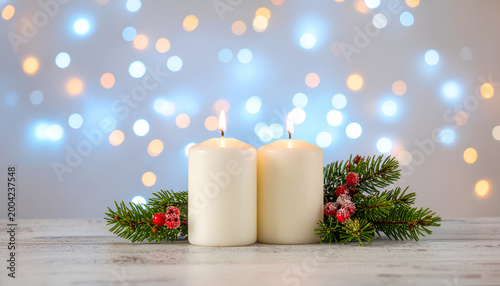 White pillar candles with evergreen pine and red berries against bokeh lights.