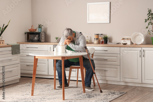 Portrait of sad senior man with tissues sitting at table in kitchen