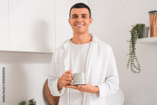 Handsome young man with cup of coffee in kitchen at home