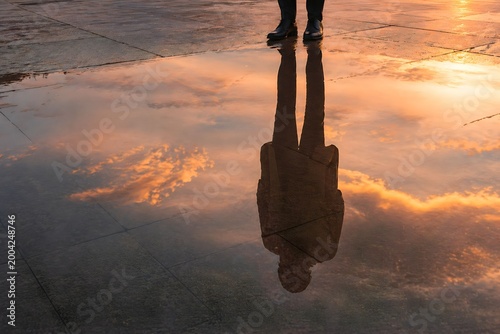 Reflection of a business person in water puddle at sunset, silhouette concept of identity and introspection