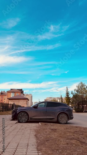 Premium sedan parked on dry grass under blue sky, gravel driveway beside suburban houses, warm spring light casting subtle