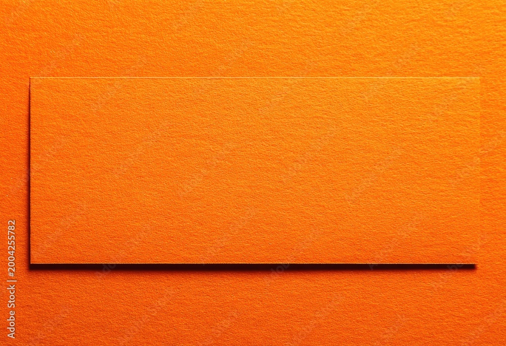 Fototapeta premium Orange card on textured orange surface with subtle shadow, top-down studio shot