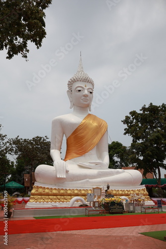 An ancient golden Buddha statue sits in peaceful meditation at a Thai temple under a blue sky, representing a sacred cultural image of Buddhist worship and religious faith in Asia