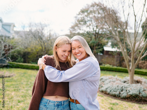 Mum hugging teenage daughter while standing in the backyard of their new home on a sunny day