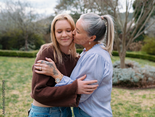 Mum hugging teenage daughter giving her a kiss on the cheek in the backyard