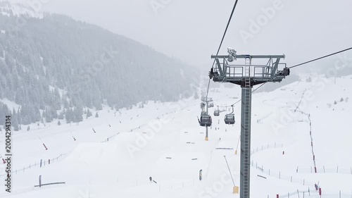 Ski lift rising above snowy slopes in Courchevel, France, surrounded by foggy alpine scenery during winter snowfall, with crowds of skiers descending the busy ski sl
