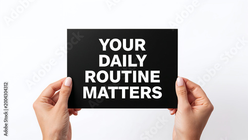 Two hands are holding a black rectangular sign with white text that says your daily routine matters very clearly