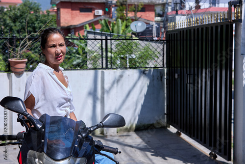 Asian woman in white top posing beside black motorcycle on rooftop courtyard bright sunlight