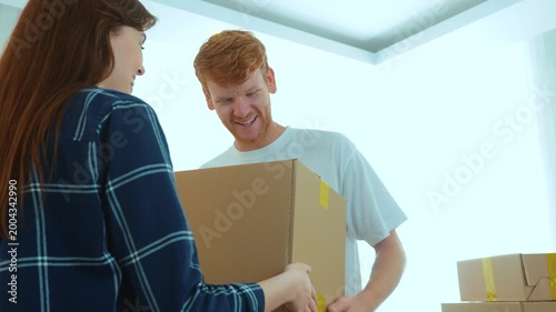 Close up of beautiful young female holding big cardboard box giving it to handsome male in light room. Caucasian couple moving in together in new home. Couple relationships. New apartment. Real time