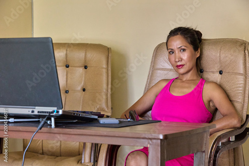 Female professional in pink top seated at desk glancing sideways from laptop screen