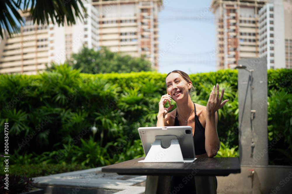 Fototapeta premium Attractive confident fit woman wearing sportswear using tablet pc computer and and speaking on phone urban park outside