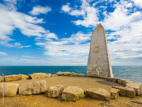 Historical stone obelisk monument serving as a coastal daymark standing against a blue sky with clouds (Portland, England, United Kingdom)
