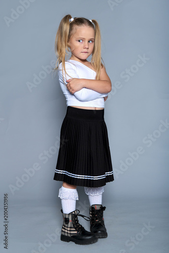 young girl gives a playful, defiant look with her arms crossed, embodying a spirited and confident attitude. Her trendy outfit and pose reflect the idea of celebrating individuality in children's
