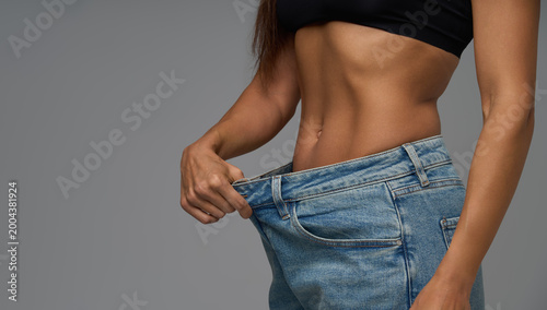 Close-up of fit woman show toned stomach in black sports bra and oversized jeans